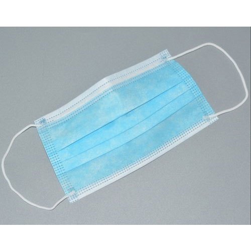 A light-blue disposable face mask lies flat on a gray surface; its ear loops are extended outward.