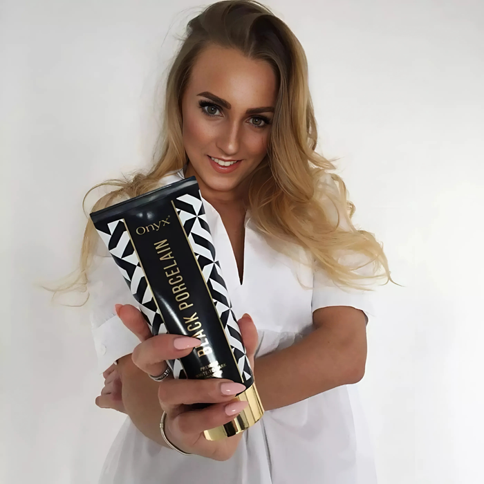 Kobieta z blond włosami prezentuje Onyx Black Porcelain. Luksusowy bronzer do opalania o formule white-to-dark.