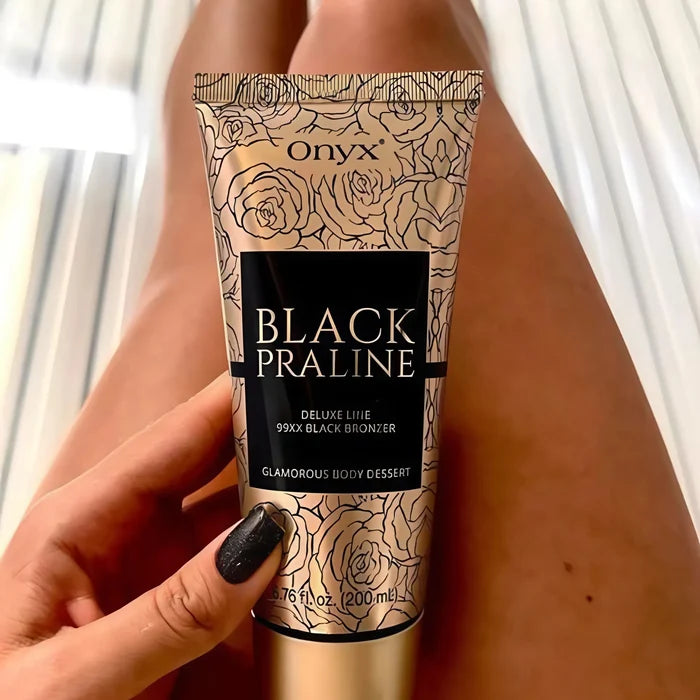Zbliżenie na dłoń kobiety trzymającej balsam Onyx Black Praline, w tle opalone nogi na łóżku w solarium