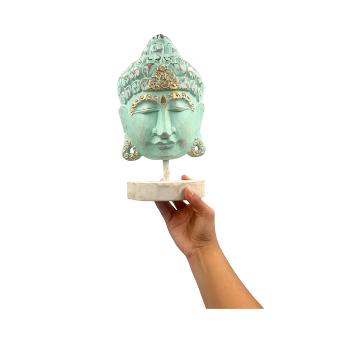 Turquoise Buddha head sculpture held by a hand on a white background
