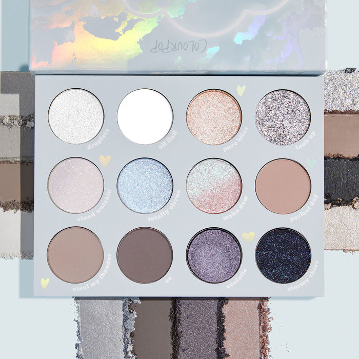 Cloud 9 ColourPop Shadow Palette opens to 12 cool‑toned shades - silvers, taupes, icy blues, and mauves - in matte, shimmer, and glitter finishes, with swatches along the edges and bottom on a pale blue background showing payoff and texture.