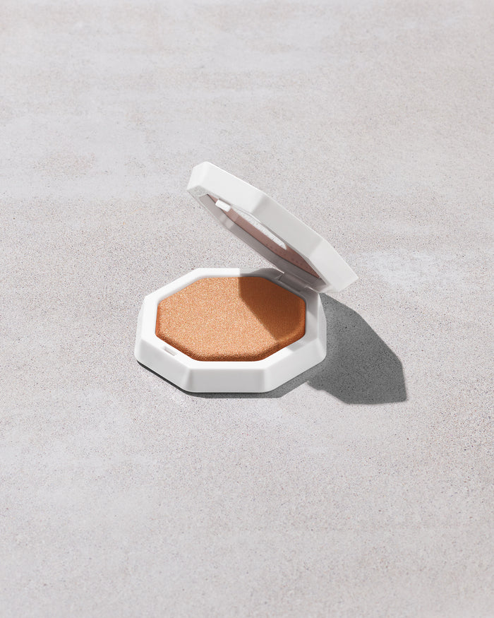 Open product shot of Demi'glow Light-Diffusing Highlighter in shade Trophies in Truffle on a concrete backdrop.