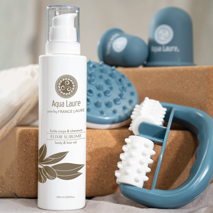 Aqua Laure Elixir Sublime body & hair oil in white pump bottle with blue massage tools, for luxurious skin and hair care routine.
