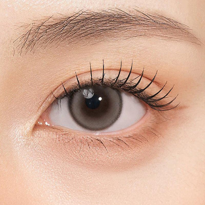 Close-up shot of model's eye adorned with Gemhour Themis Nude Grey color contact lenses with prescription, complemented by minimalist eye makeup, showing the brightening and enlarging effect of the circle contact lens on dark brown eyes.