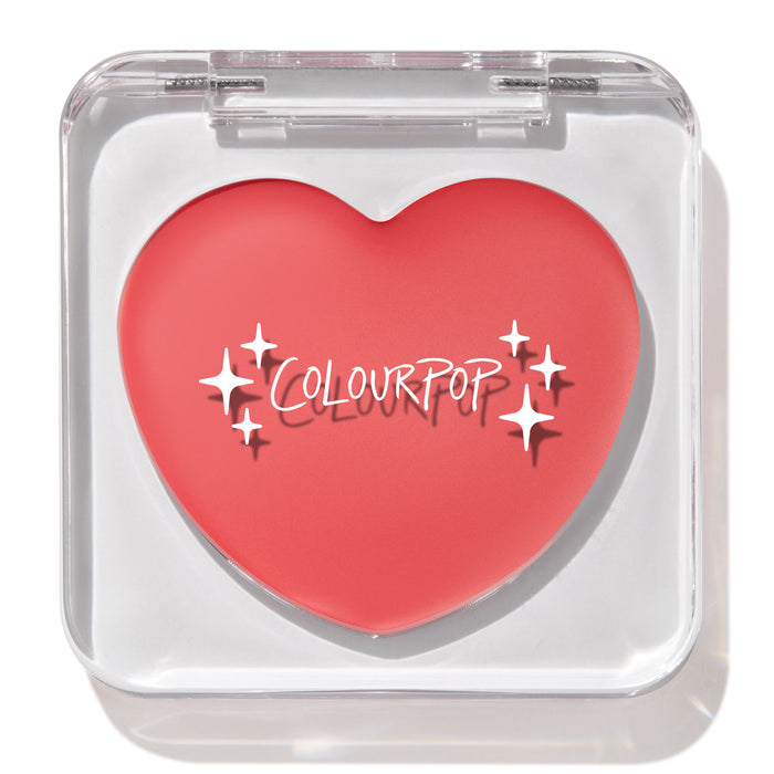 Heart-shaped ColourPop Lip and Cheek Balm in It’s a Look resting in a clear square compact with lid closed, showcasing a warm coral-pink shade and white ColourPop logo on a clean white background.