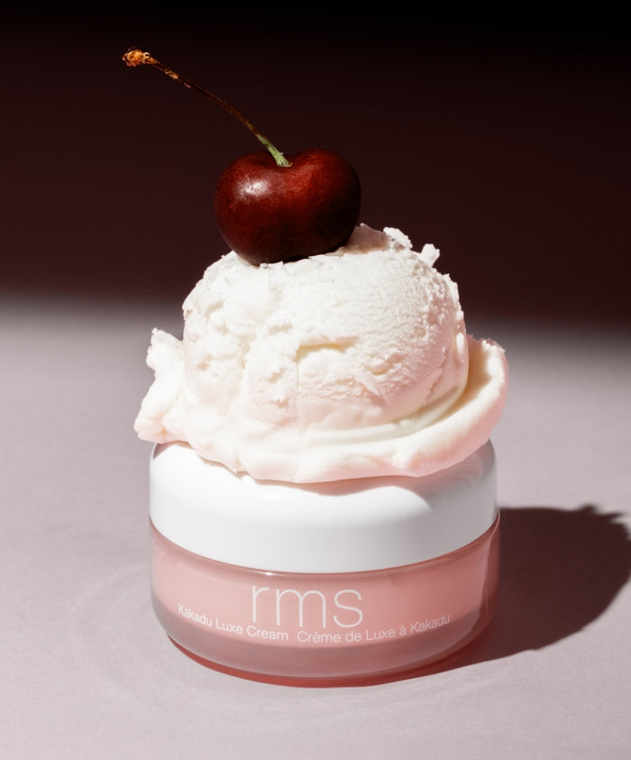 Kakadu Luxe Cream jar with a scoop of creamy white texture topped with a fresh cherry, highlighting natural ingredients and luxurious skincare.