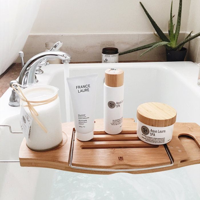 France Laure skincare products on bamboo bath tray: illuminating almond exfoliant, spa gel, and dermo-performance butter for luxurious self-care