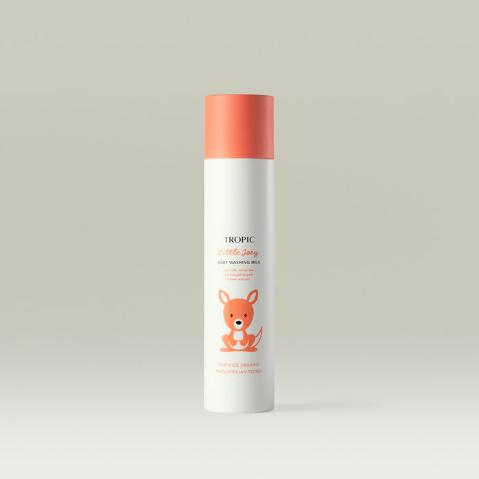 Tropic Little Joey Baby Washing Milk bottle with coral-orange cap and cute kangaroo illustration on a light background. Text mentions oat milk, white tea, and kangaroo paw flower extract.