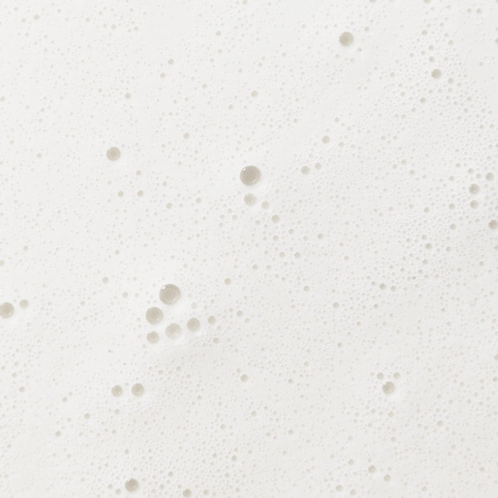 Close-up of a creamy white foamy texture with fine bubbles, representing the gentle formula of baby washing milk.
