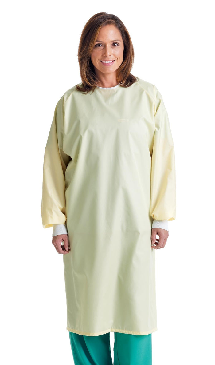 A woman stands wearing a pale yellow, long-sleeved gown against a white background.