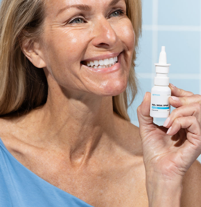 Woman holding a NAD+ nasal spray bottle with a blue background