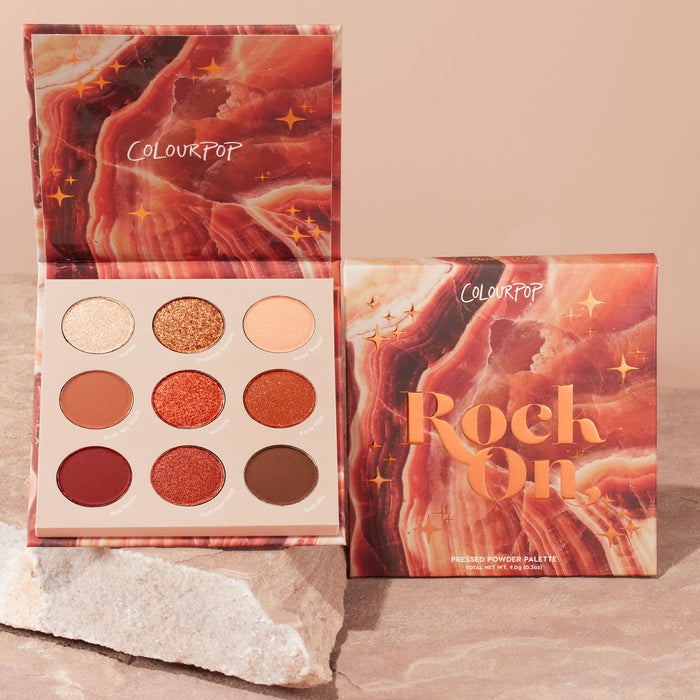 Rock On ColourPop Shadow Palette displaying nine pressed powder shades - champagne, gold glitter, peach, terracotta, copper, rust, wine, rose, and deep brown - opened next to its marbled box on a stone surface.