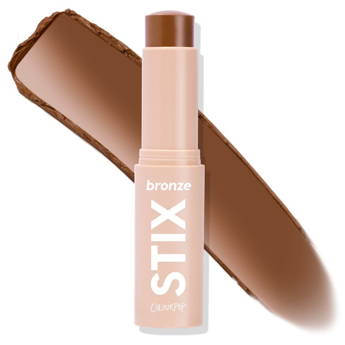 ColourPop Bronzer Stix Shell Beach stands uncapped in a nude tube labeled STIX, revealing a warm medium-brown cream stick, with a wide bronzer swatch behind on a white background.