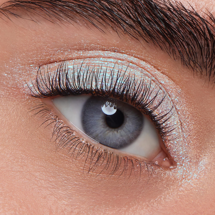 Eye wearing ColourPop Jelly Much Shadow in Super Cool, an icy blue iridescent shimmer swept across the lid and inner corner, shown in a macro close-up with long lashes and a defined brow under studio lighting.